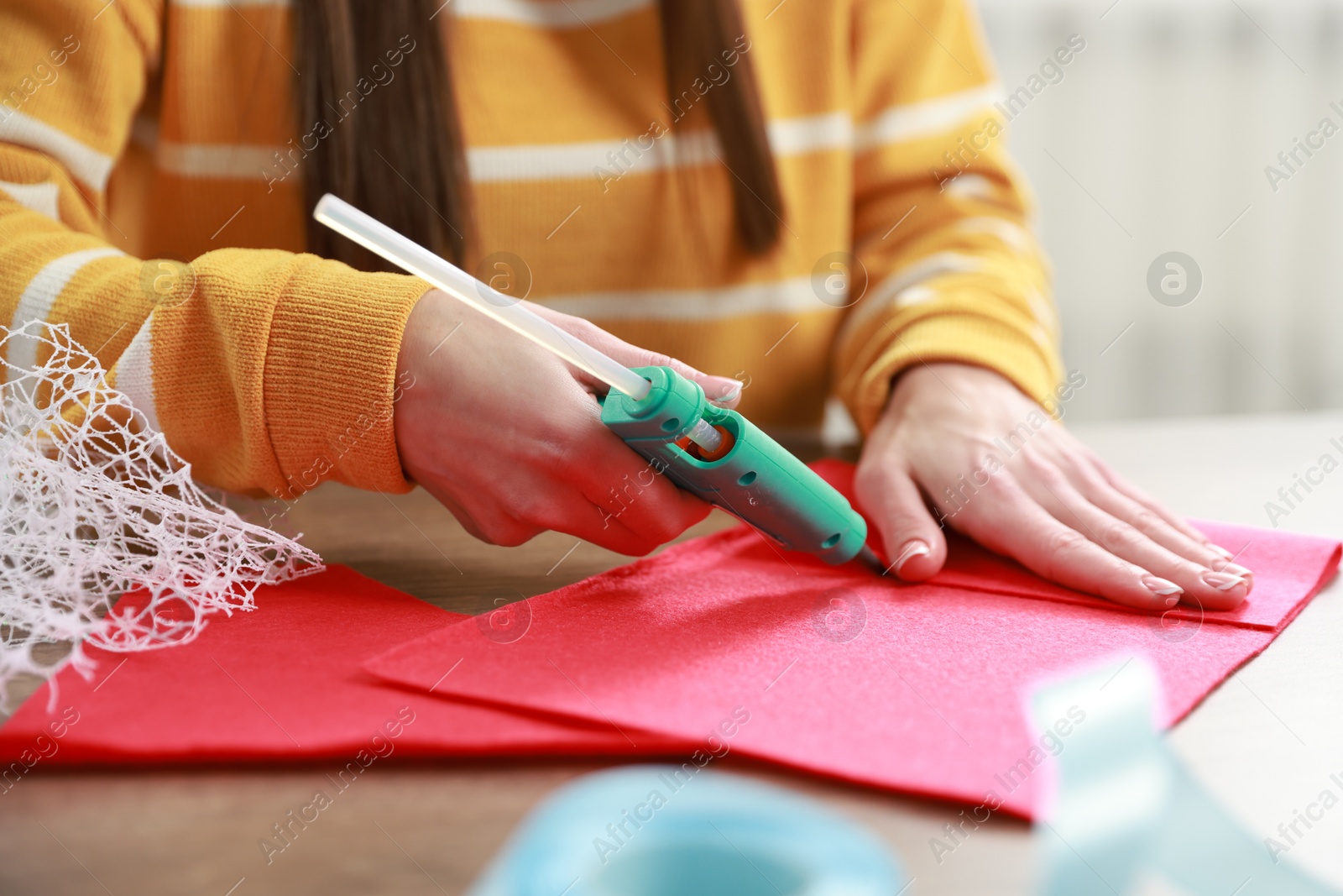 Photo of Woman with hot glue gun making craft at table indoors, closeup