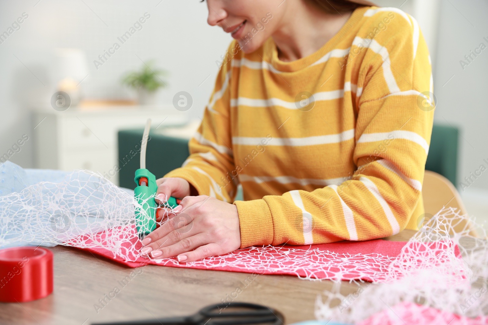 Photo of Woman with hot glue gun making craft at table indoors, closeup