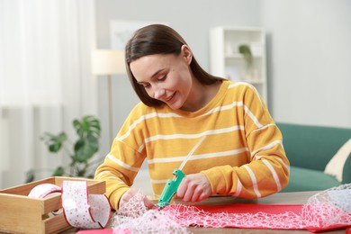 Photo of Woman with hot glue gun making craft at table indoors