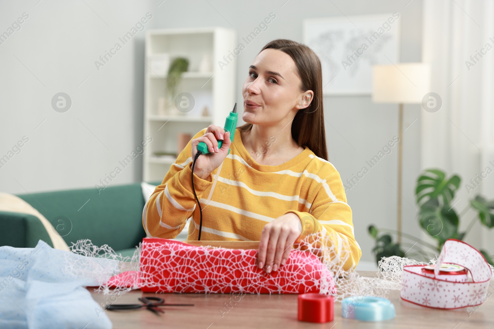 Photo of Woman with hot glue gun making craft at table indoors