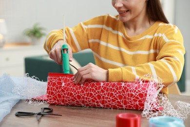 Photo of Woman with hot glue gun making craft at table indoors, closeup