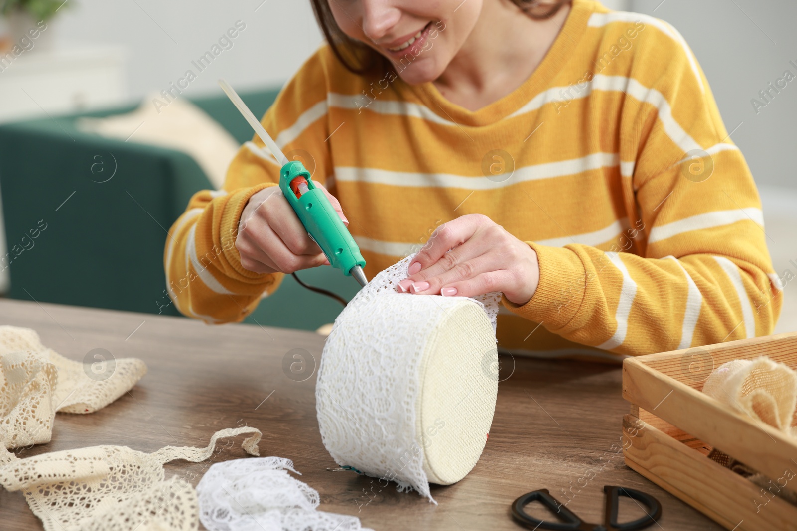 Photo of Woman with hot glue gun making craft at table indoors, closeup