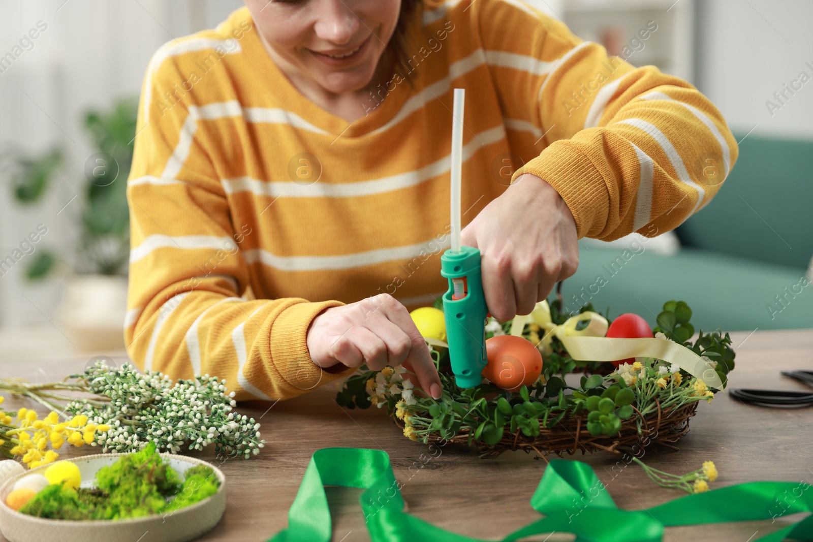 Photo of Woman with hot glue gun making craft at table indoors, closeup