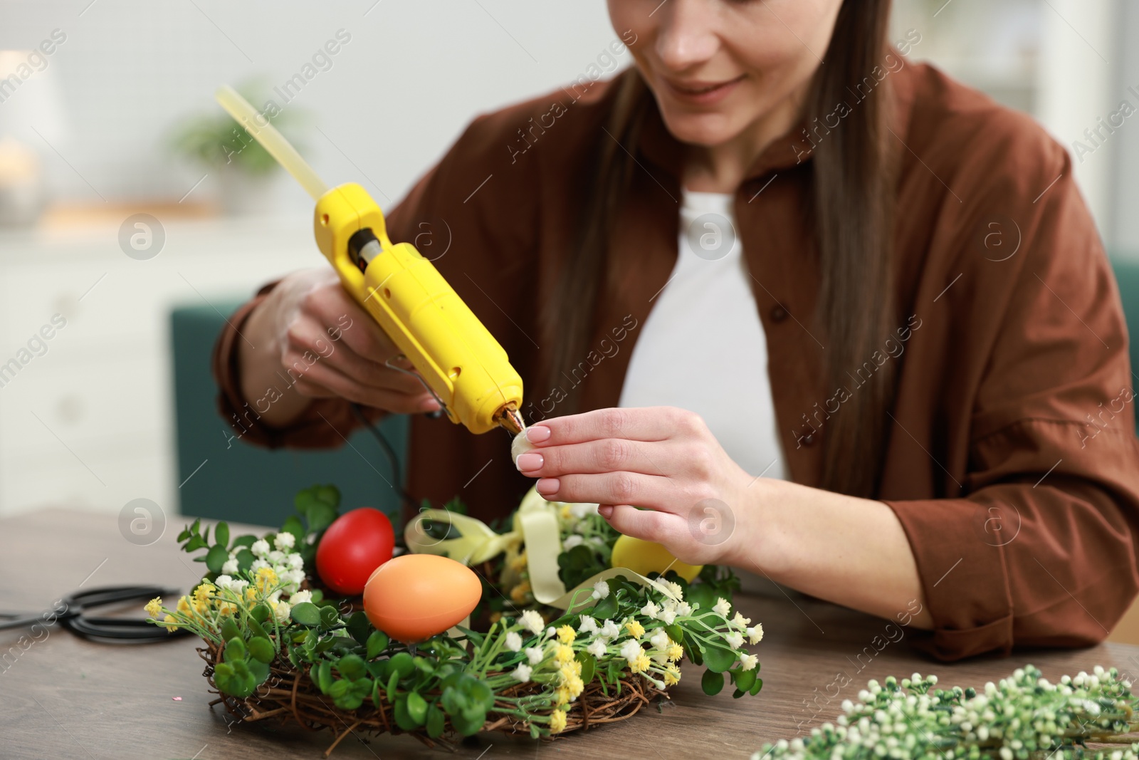 Photo of Woman with hot glue gun making craft at table indoors, closeup