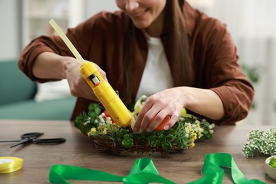 Photo of Woman with hot glue gun making craft at table indoors, closeup