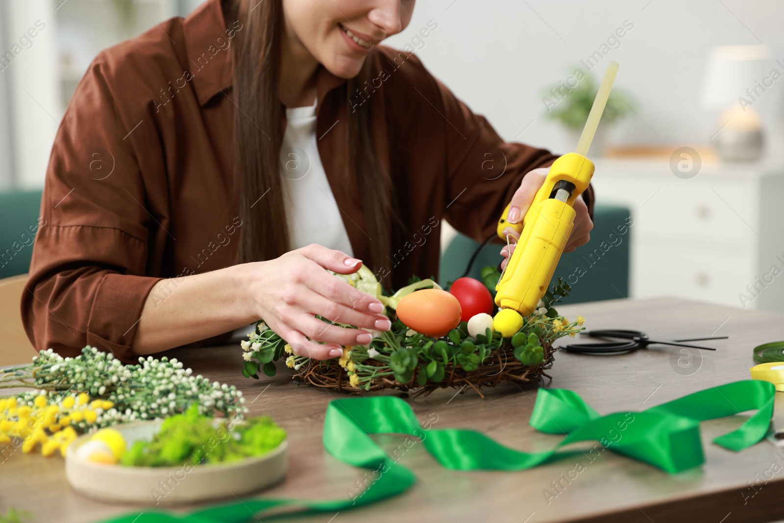 Photo of Woman with hot glue gun making craft at table indoors, closeup