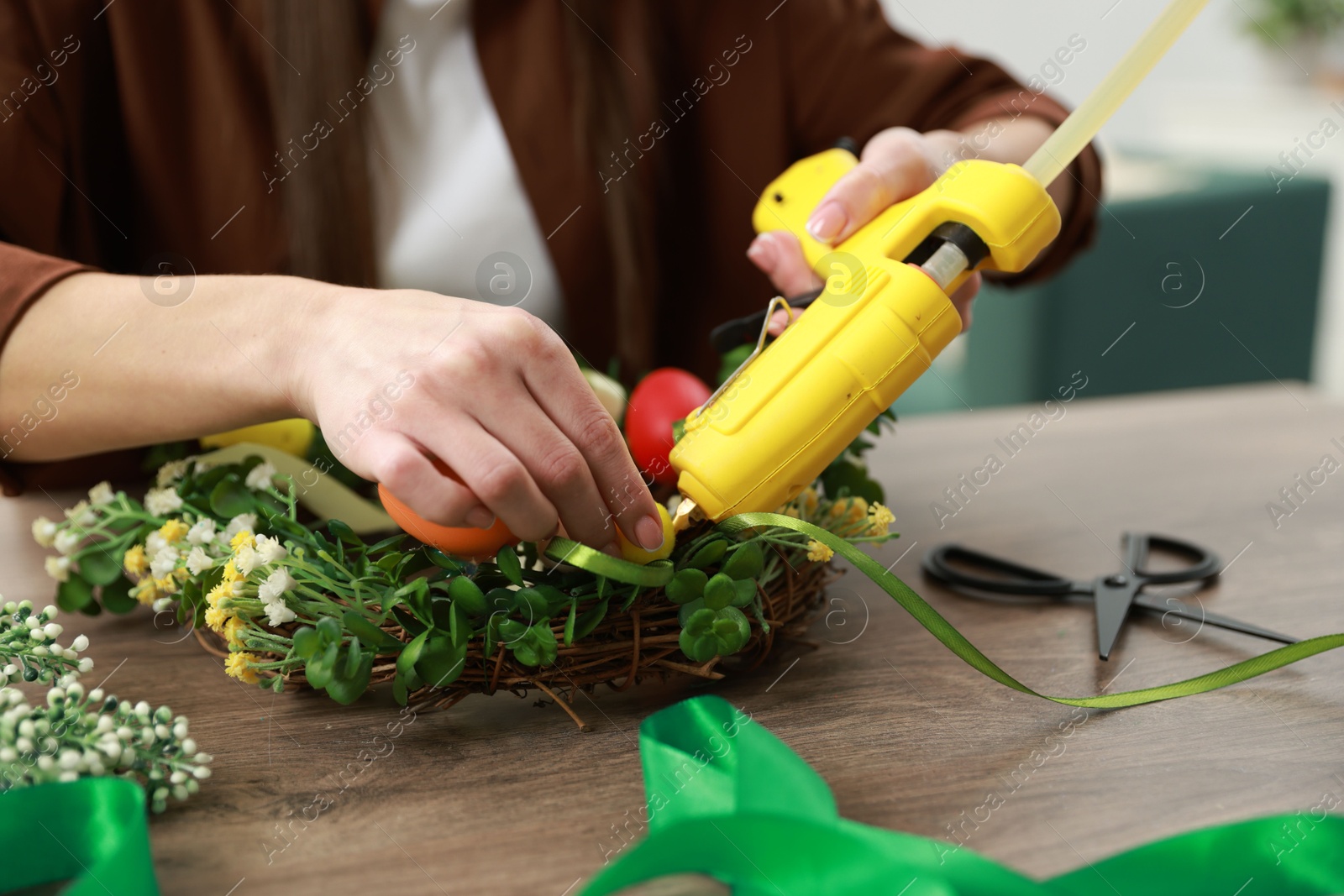 Photo of Woman with hot glue gun making craft at table indoors, closeup