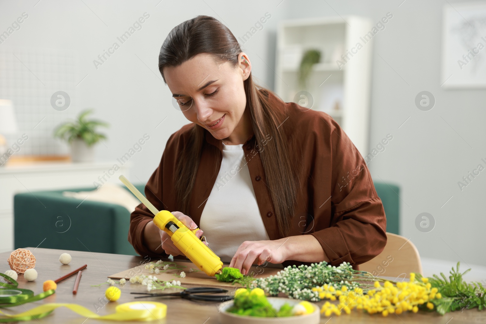 Photo of Woman with hot glue gun making craft at table indoors