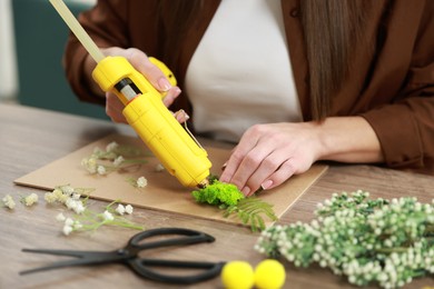 Photo of Woman with hot glue gun making craft at table indoors, closeup