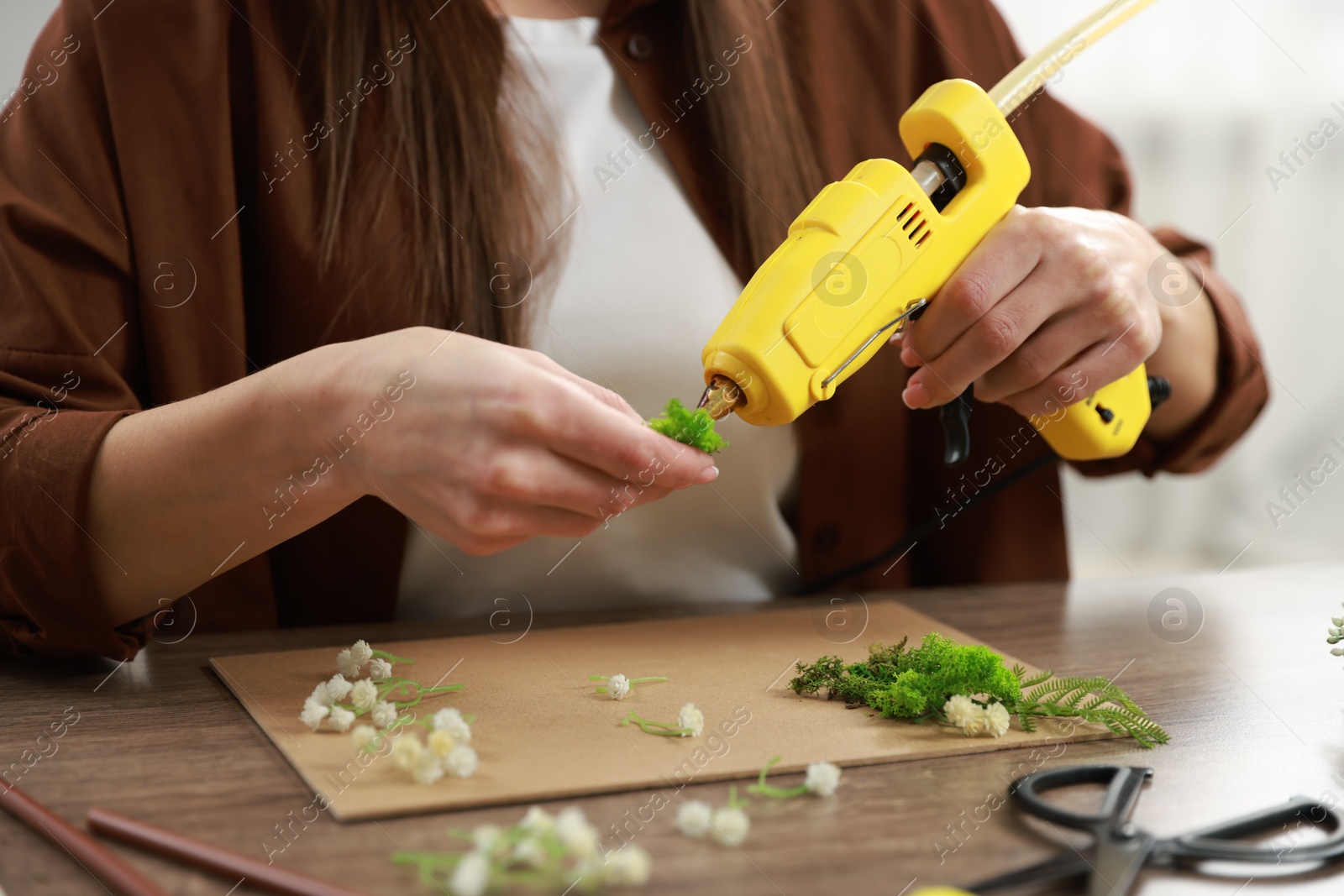 Photo of Woman with hot glue gun making craft at table indoors, closeup