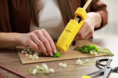 Photo of Woman with hot glue gun making craft at table indoors, closeup