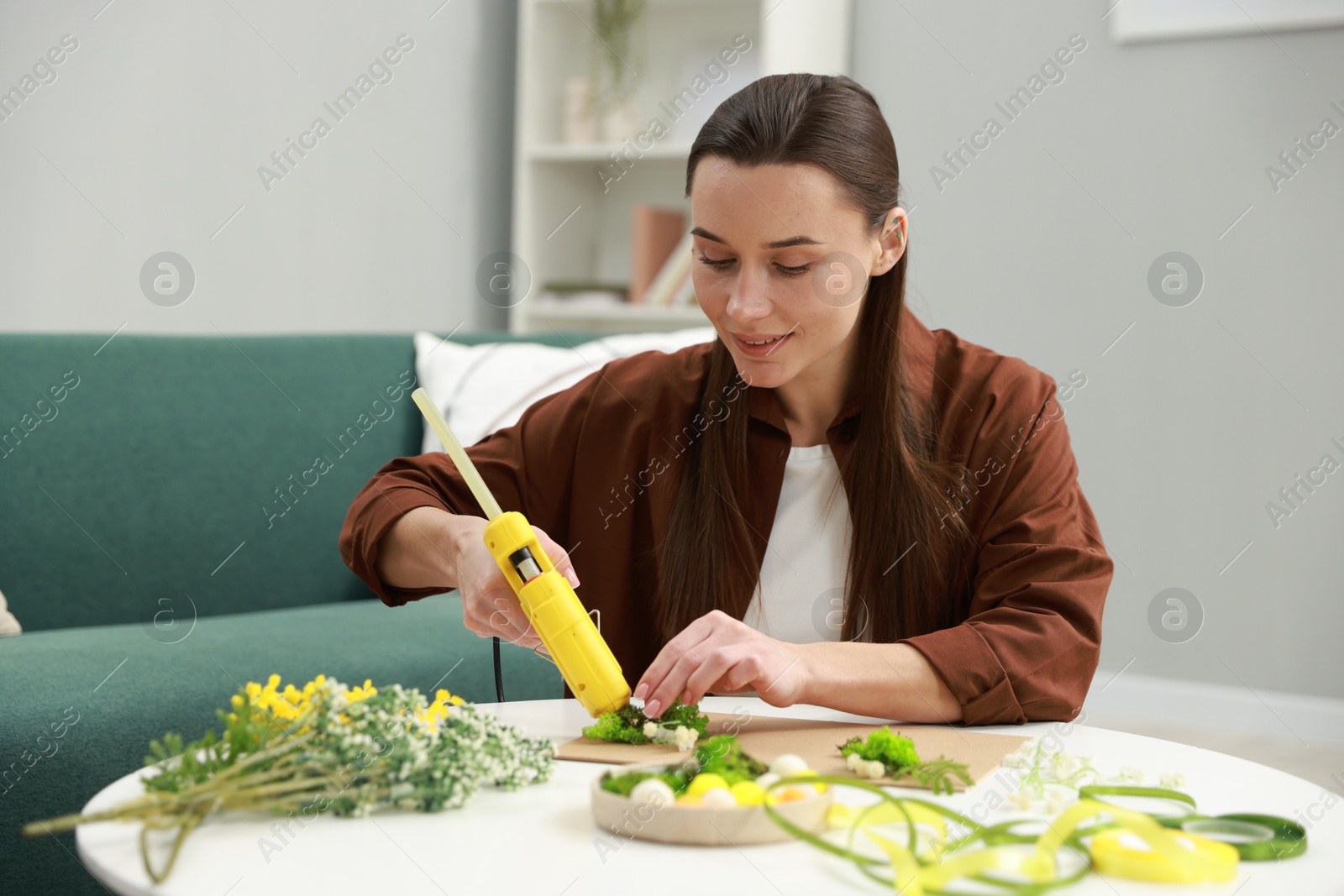 Photo of Woman with hot glue gun making craft at table indoors