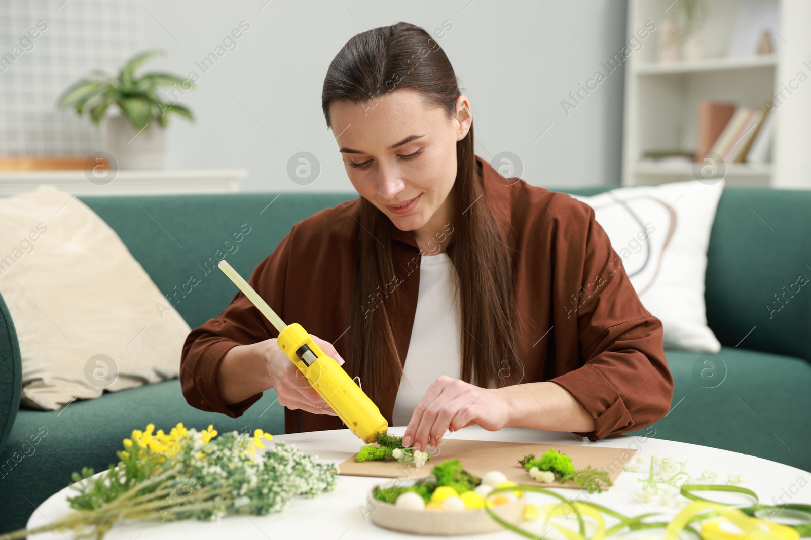 Photo of Woman with hot glue gun making craft at table indoors