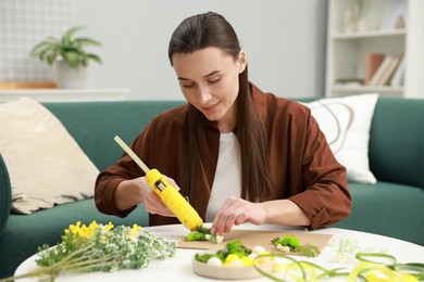 Photo of Woman with hot glue gun making craft at table indoors