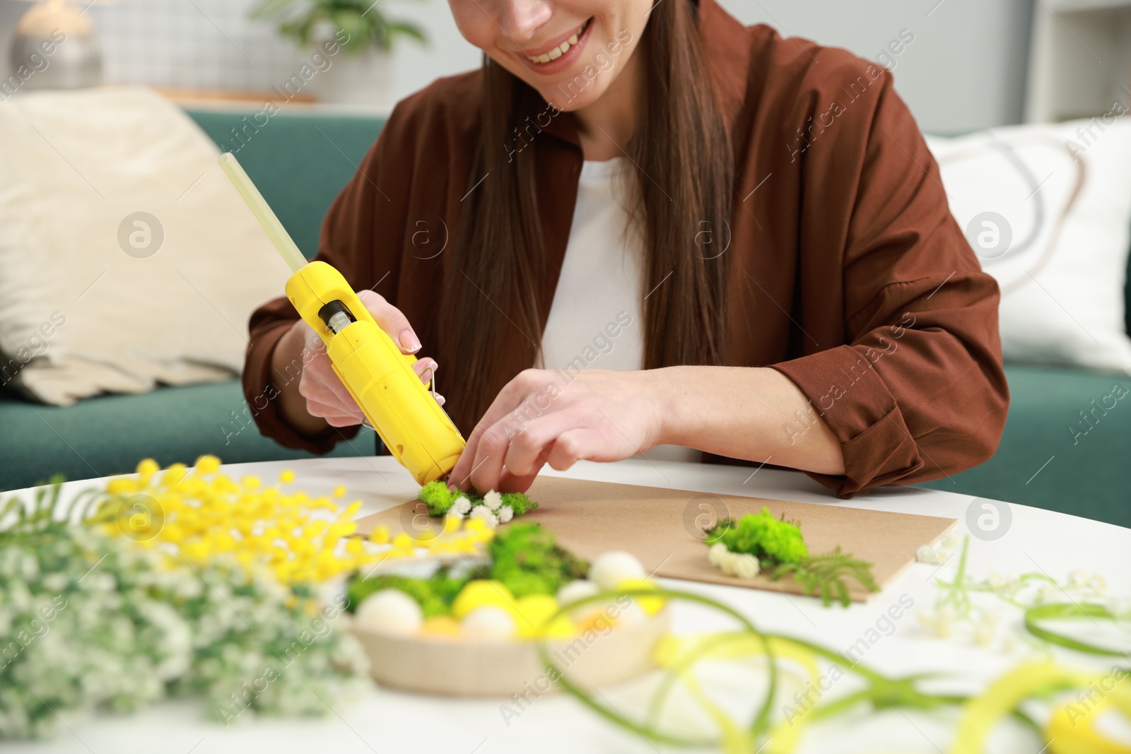 Photo of Woman with hot glue gun making craft at table indoors, closeup