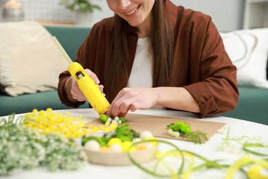 Photo of Woman with hot glue gun making craft at table indoors, closeup