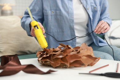 Photo of Woman with hot glue gun making craft at table indoors, closeup