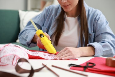 Photo of Woman with hot glue gun making craft at table indoors, closeup