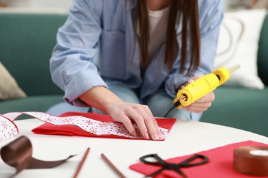 Photo of Woman with hot glue gun making craft at table indoors, closeup