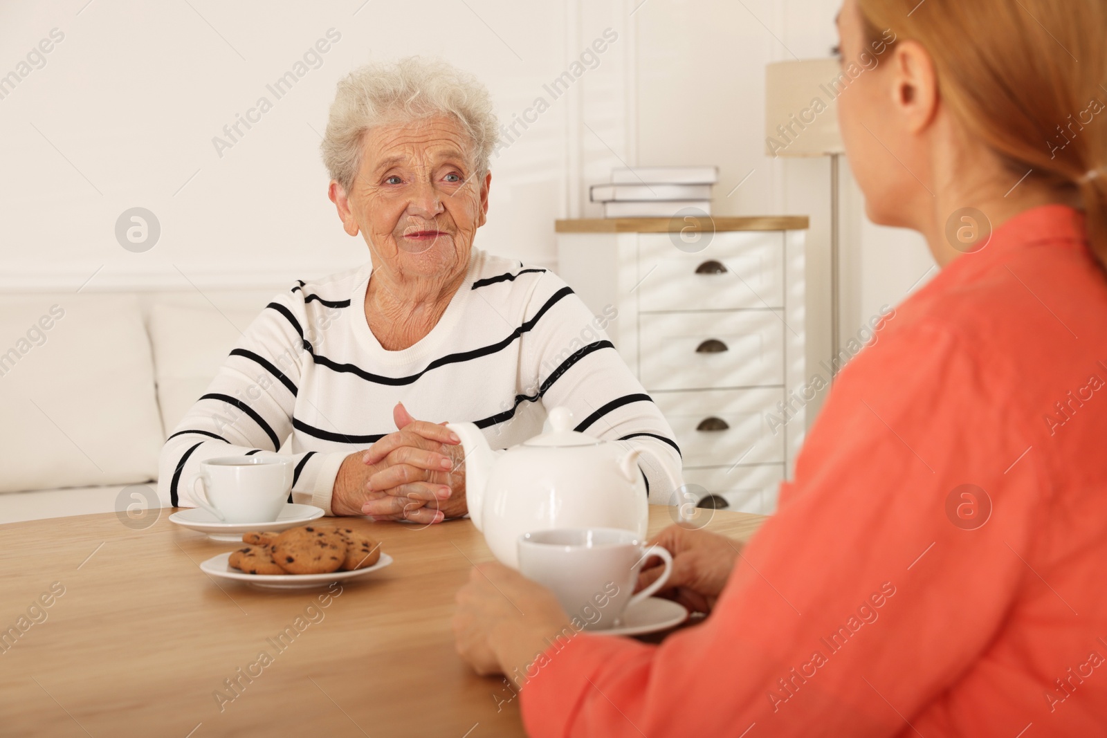 Photo of Caregiver and senior woman enjoying hot drink at table indoors