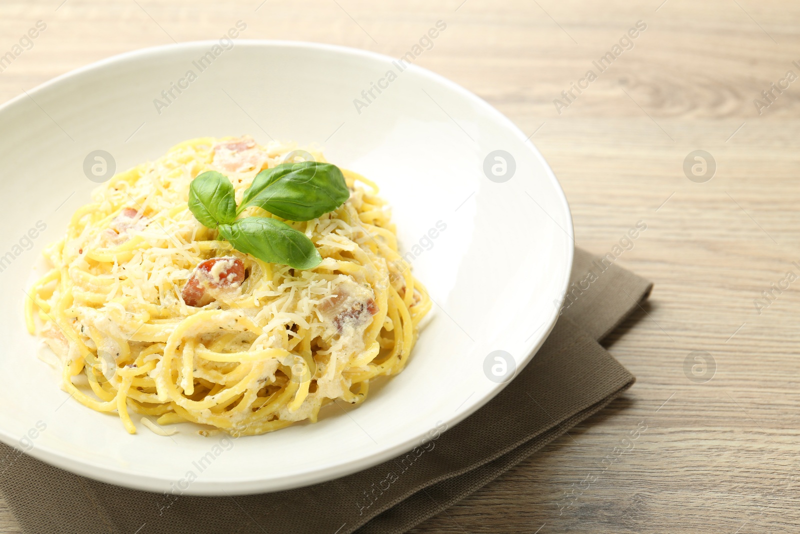 Photo of Delicious pasta Carbonara in bowl on wooden table, closeup