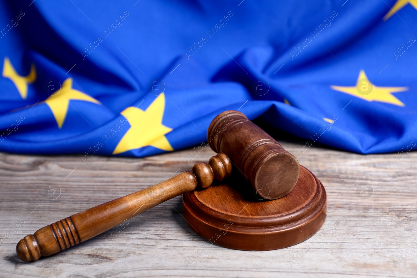 Photo of Judge's gavel and European Union flag on wooden table, closeup