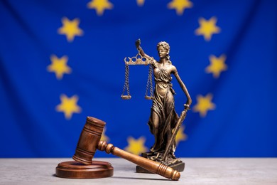 Photo of Figure of Lady Justice and judge's gavel on table against European Union flag