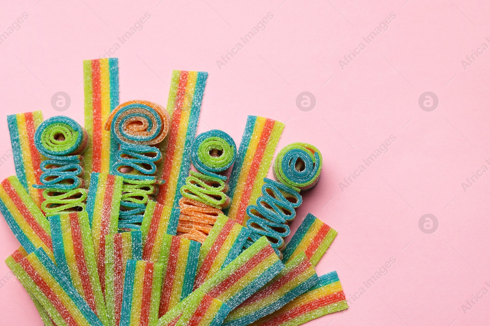 Photo of Tasty rainbow sour belts on pink background, top view