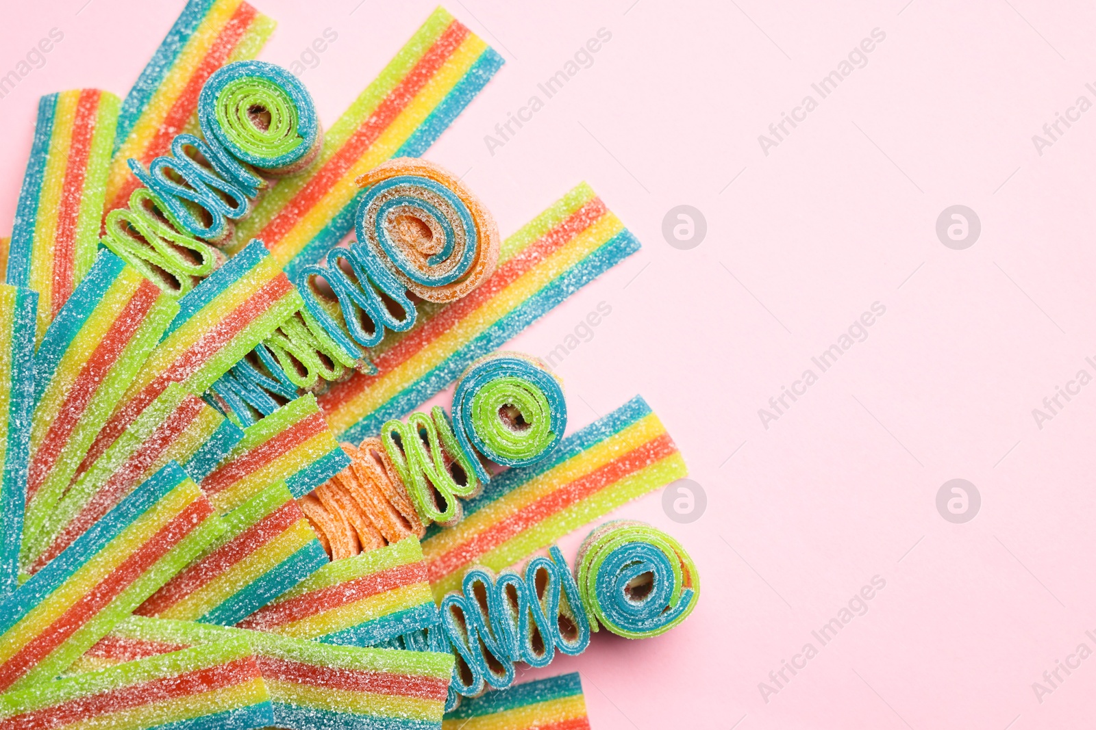 Photo of Tasty rainbow sour belts on pink background, top view. Space for text