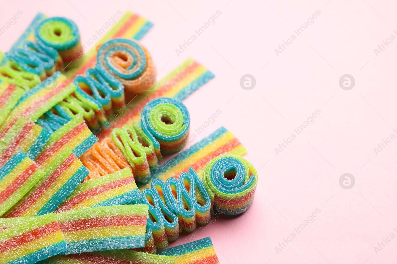 Photo of Tasty rainbow sour belts on pink background, closeup. Space for text