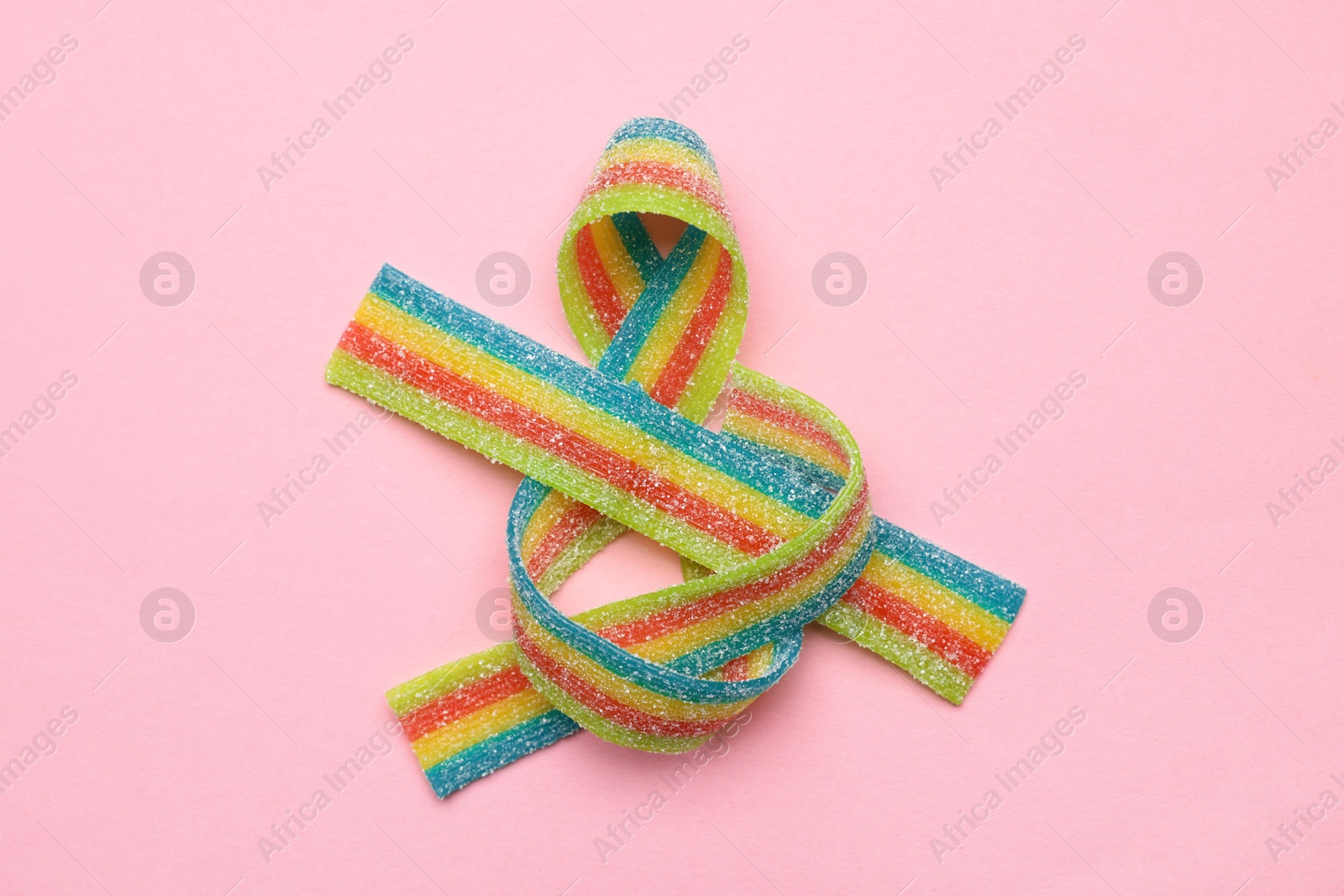 Photo of Tasty rainbow sour belts on pink background, top view