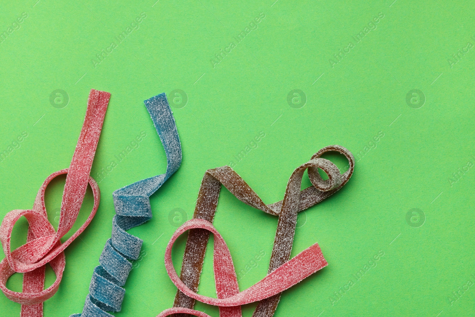 Photo of Different tasty sour belts on green background, flat lay