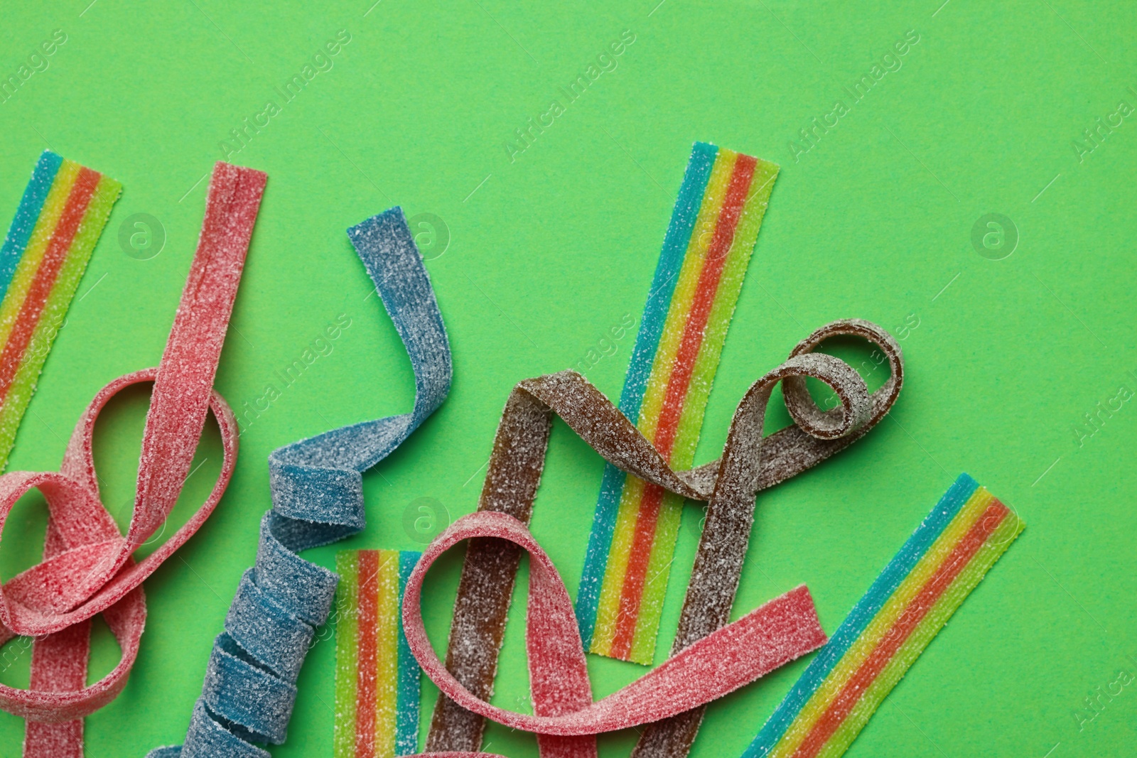 Photo of Different tasty sour belts on green background, flat lay