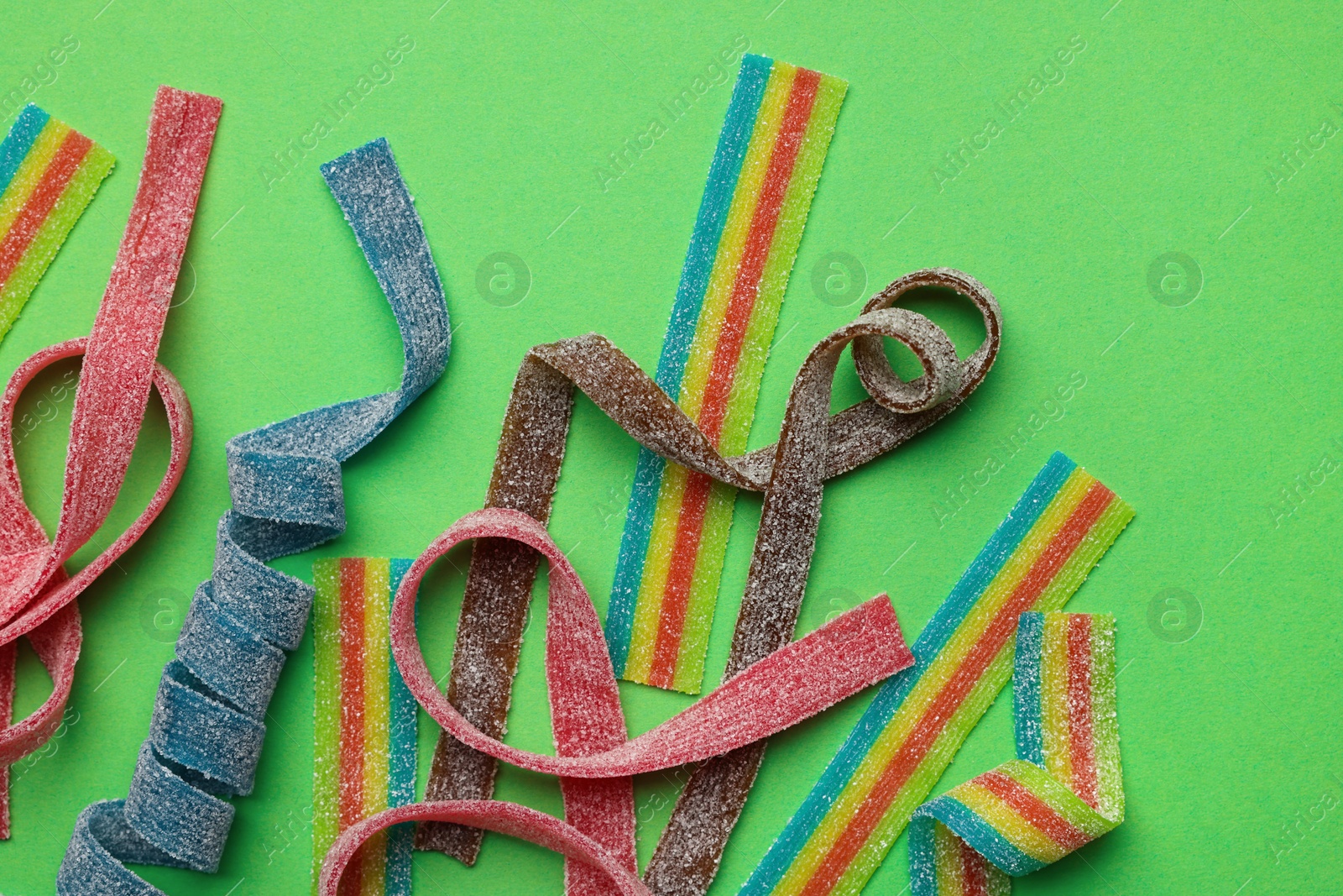 Photo of Different tasty sour belts on green background, flat lay