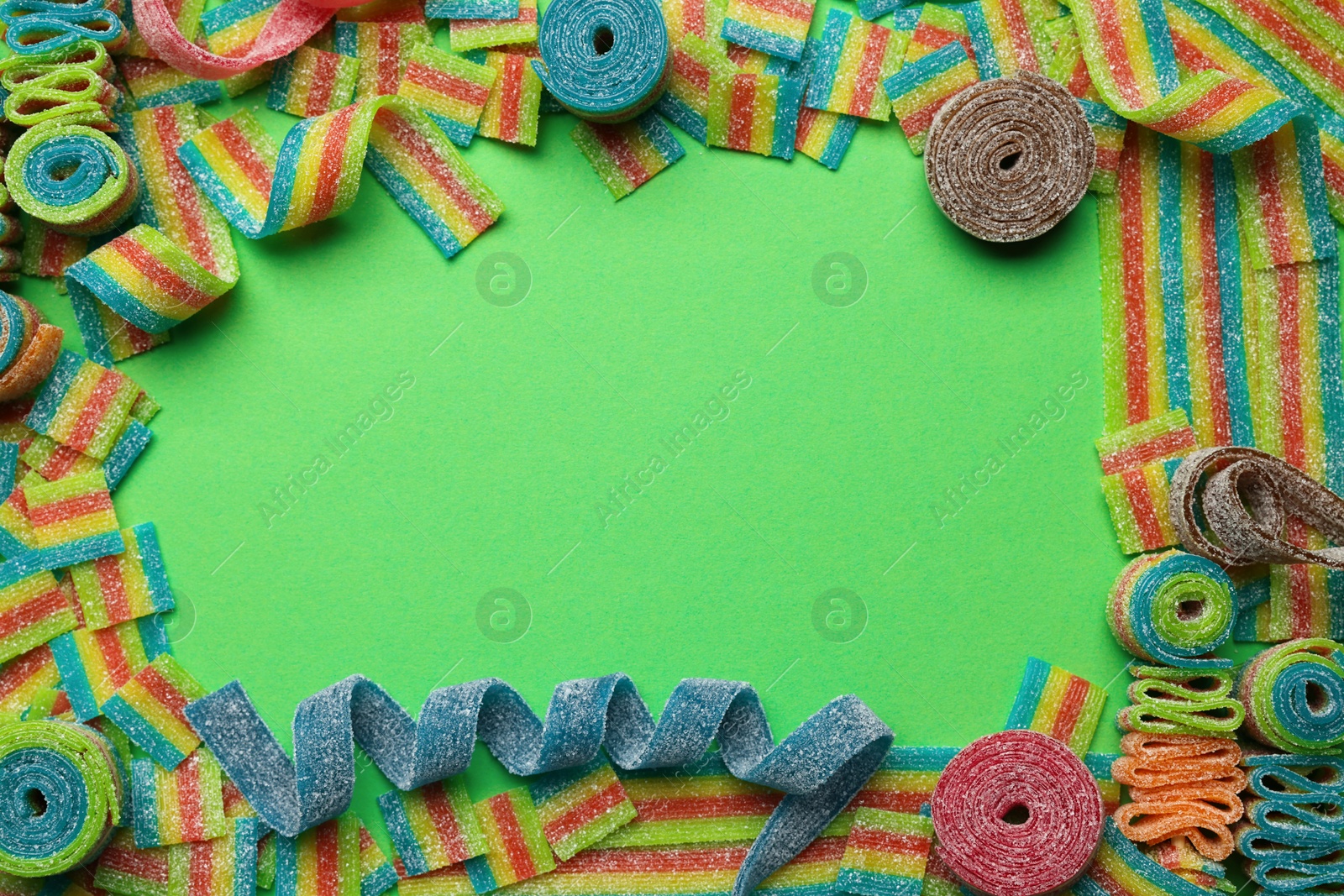 Photo of Frame of different tasty sour belts on green background, flat lay. Space for text