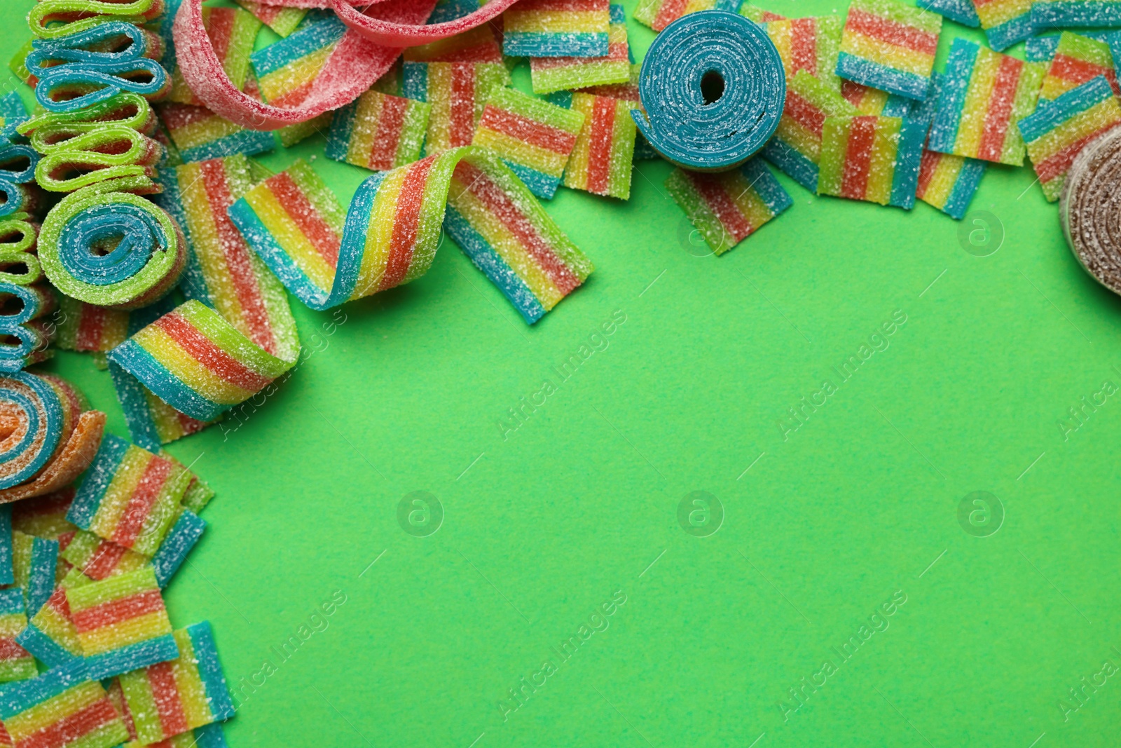 Photo of Different tasty sour belts on green background, flat lay. Space for text