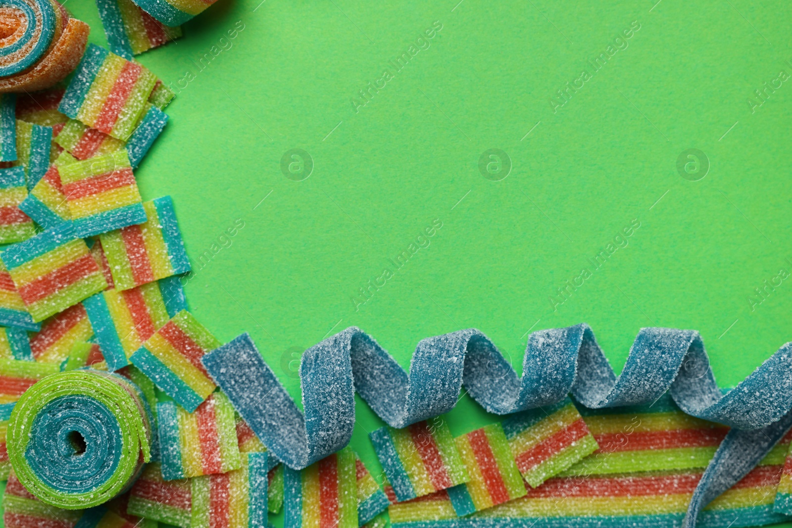 Photo of Different tasty sour belts on green background, flat lay. Space for text