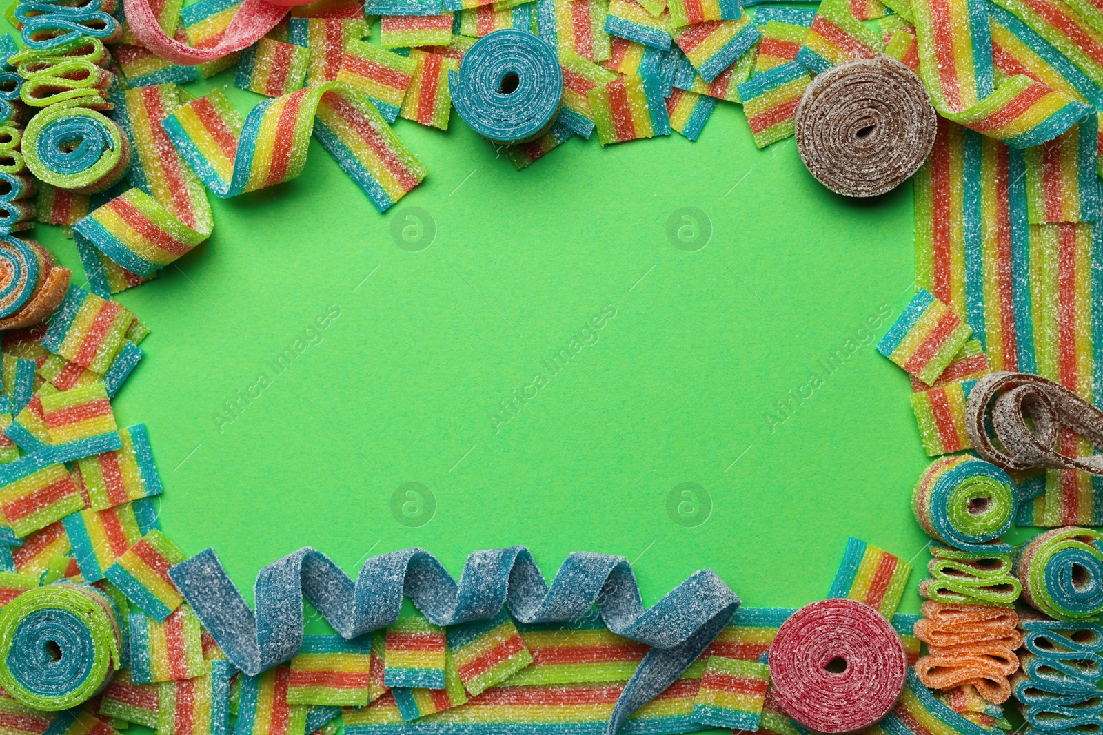 Photo of Frame of different tasty sour belts on green background, flat lay. Space for text