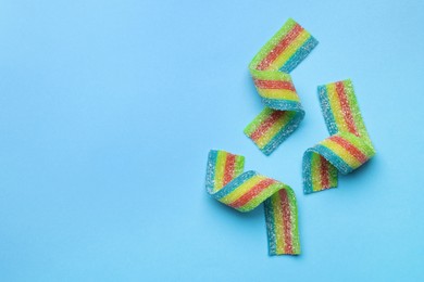 Photo of Tasty rainbow sour belts on light blue background, flat lay. Space for text