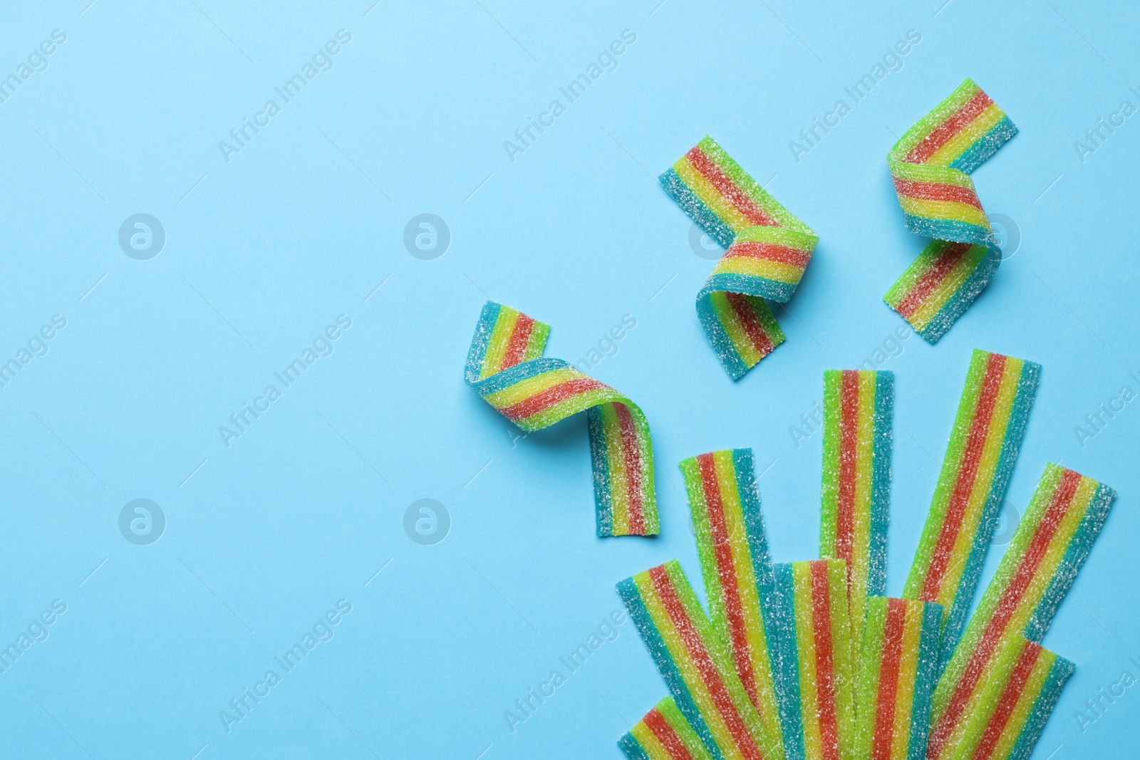 Photo of Tasty rainbow sour belts on light blue background, flat lay. Space for text