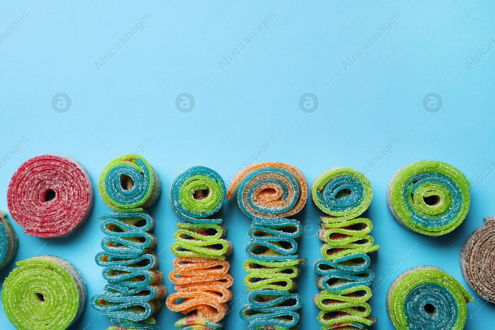 Photo of Different tasty sour belts on light blue background, flat lay. Space for text