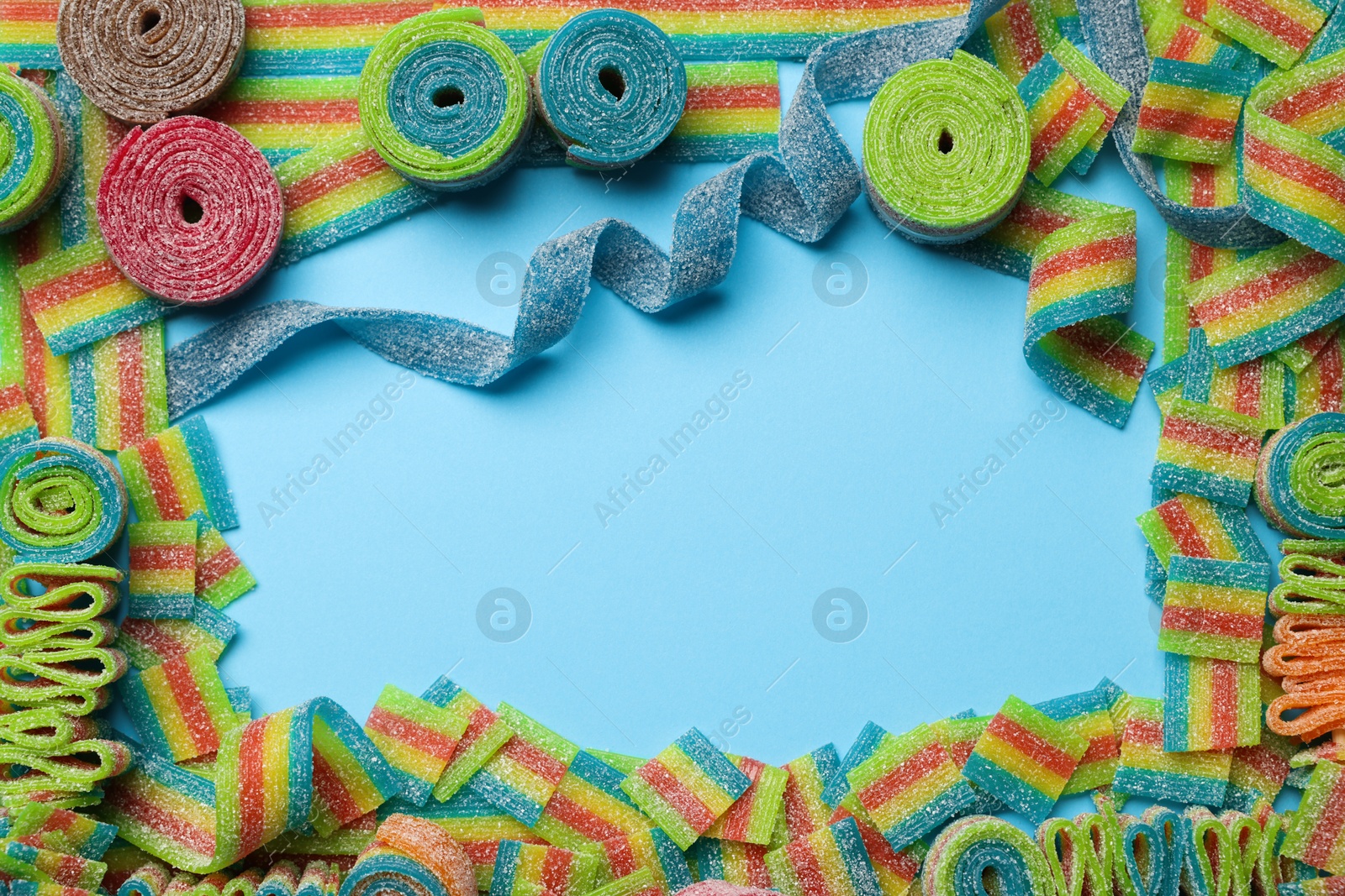 Photo of Frame of different tasty sour belts on light blue background, flat lay. Space for text