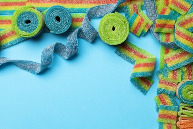 Photo of Different tasty sour belts on light blue background, flat lay. Space for text