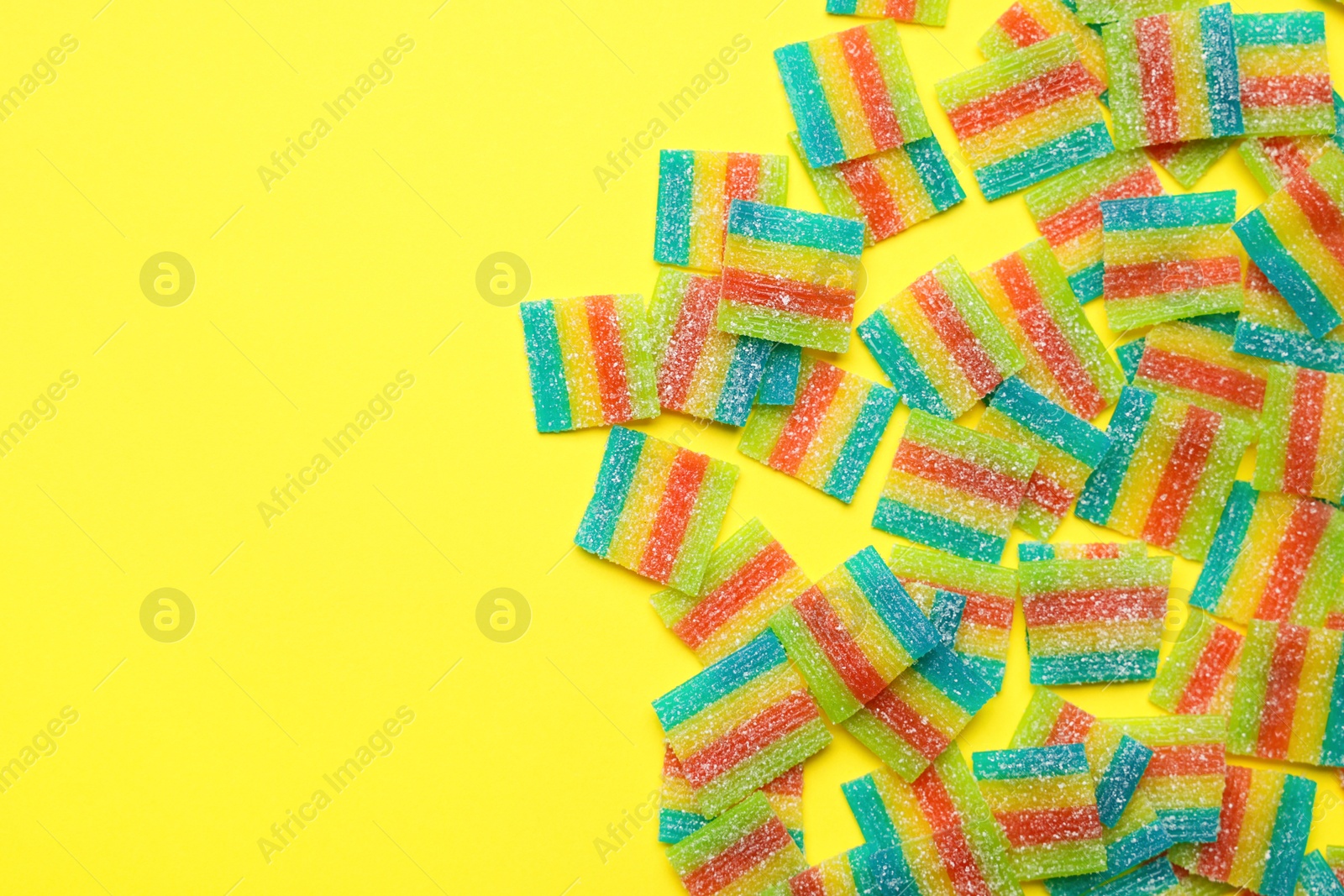 Photo of Tasty rainbow sour belts on yellow background, top view. Space for text