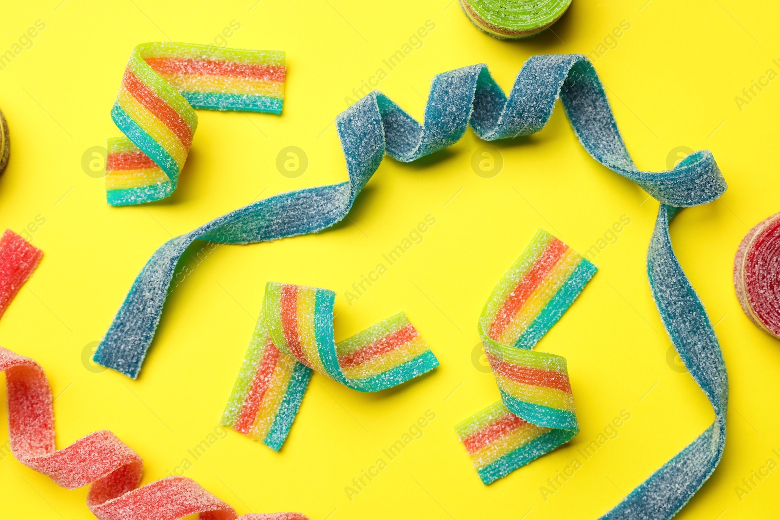 Photo of Different tasty sour belts on yellow background, flat lay