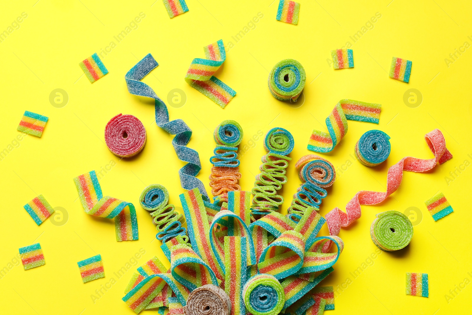 Photo of Different tasty sour belts on yellow background, flat lay