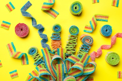 Photo of Different tasty sour belts on yellow background, flat lay