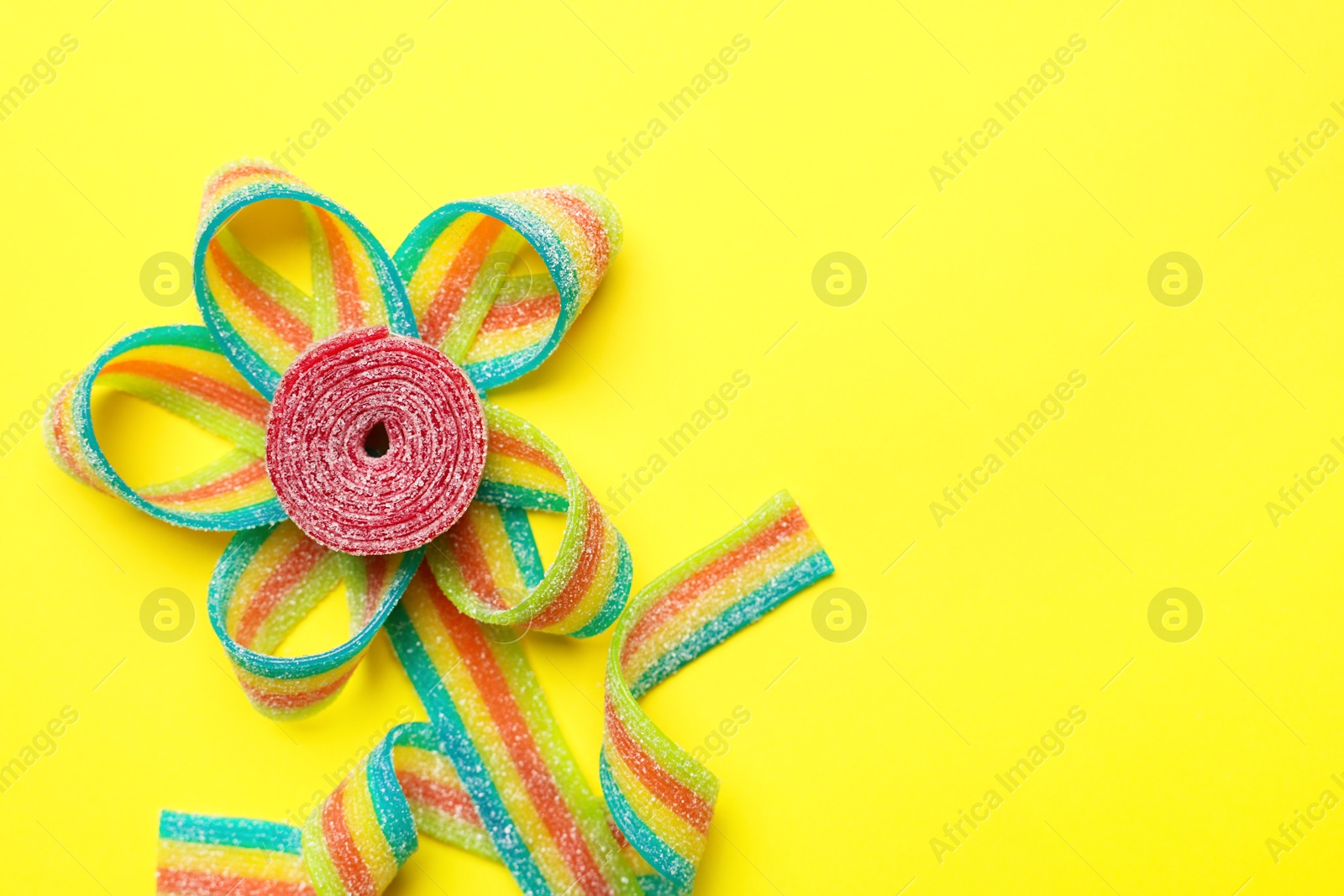 Photo of Flower made of tasty sour belts on yellow background, top view. Space for text