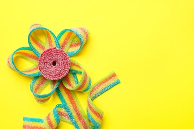 Photo of Flower made of tasty sour belts on yellow background, top view. Space for text