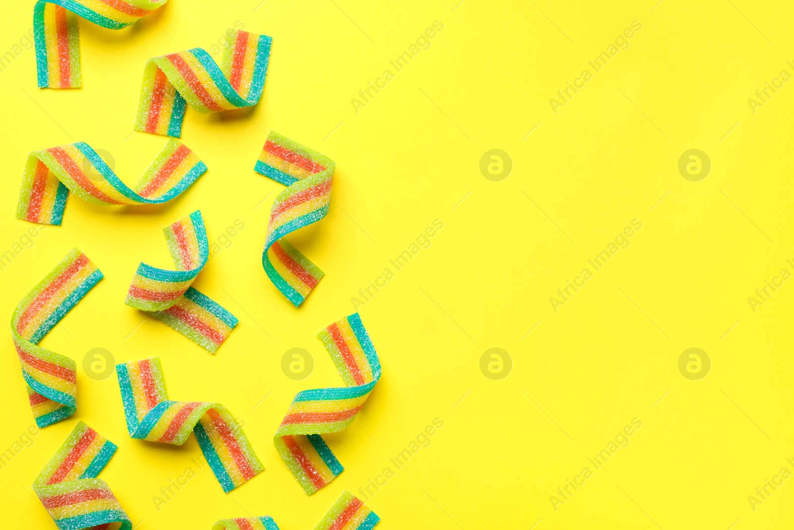 Photo of Tasty rainbow sour belts on yellow background, top view. Space for text